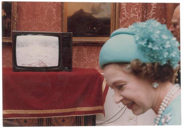 La reine Elizabeth observant la foule, venue nombreuse, sur un écran de télévision