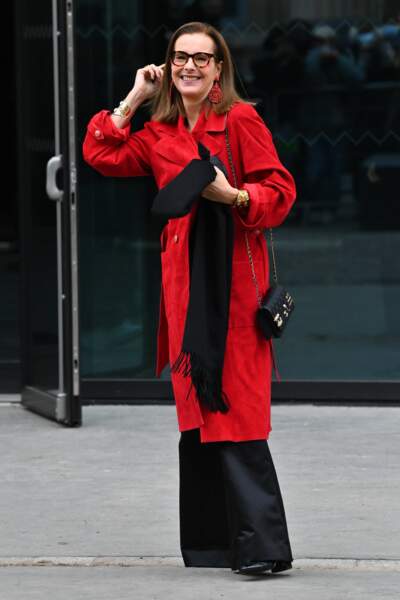 Carole Bouquet drapée dans un long manteau rouge accessoirisé de l'indispensable sac Chanel