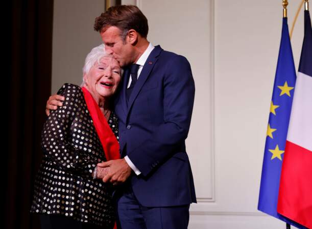 Emmanuel Macron embrassant Line Renaud sur le front après l'avoir décorée de la Grand-croix de la Légion d'honneur